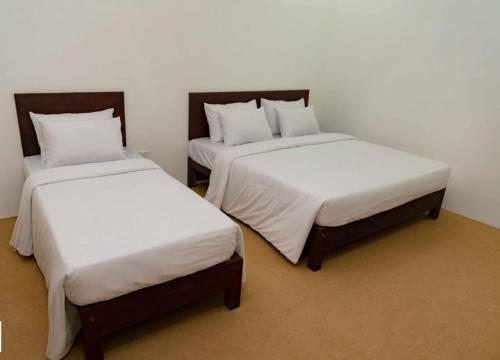 two beds in a room with white sheets at BTI Leisure Hotel in Kataragama
