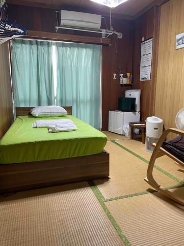a bedroom with a bed with green sheets and a chair at Adventure Hostel う島や in Iriomote