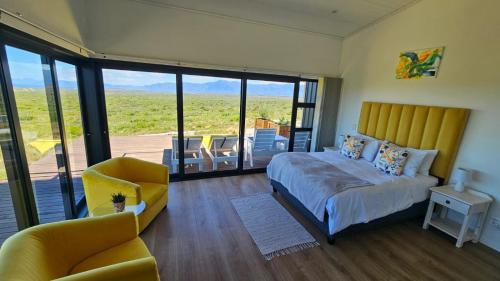 a bedroom with a bed and a balcony with chairs at Walkerbay Dunes Lodge in Stanford