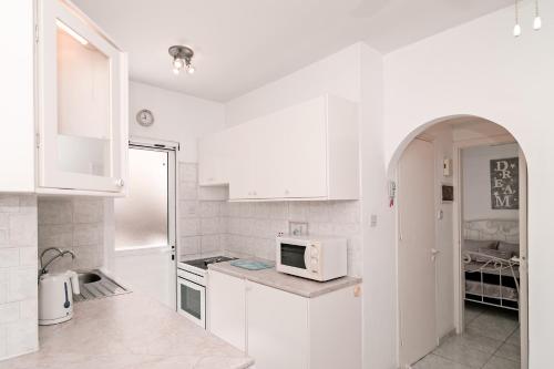 uma cozinha com armários brancos e um micro-ondas em Sue's Apartment em Pafos