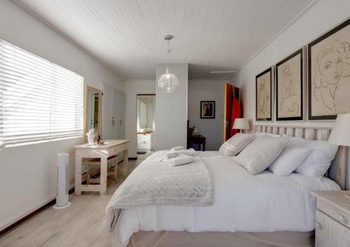 a bedroom with a large white bed and a desk at Corner Delight at Onrust Beach in Hermanus