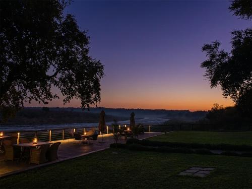 a sunset with tables and chairs and a river at Buckler's Africa Lodge Kruger Park in Komatipoort