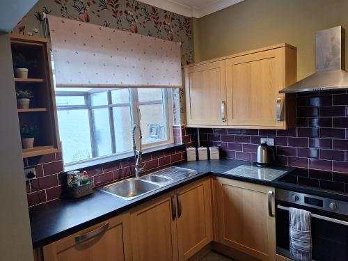 a kitchen with wooden cabinets and a sink and a window at The Hampton Beautiful 3 Bedroom House with Conservatory & Garden in Scarborough