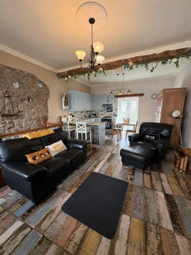 a living room with black leather furniture and a stone wall at The Old Shop Cottage, Llandudno in Penrhyn Bay