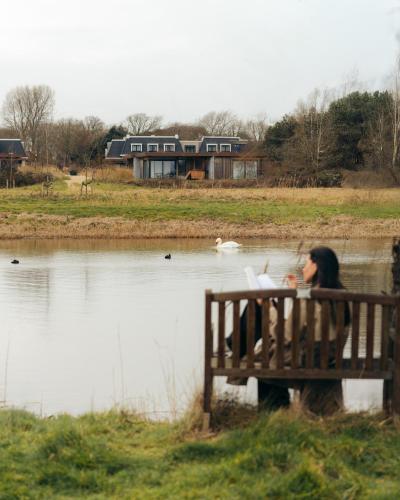 a woman sitting on a bench next to a lake at Garden Suites with Private Hottub - Duinhotel in Burgh-Haamstede zeeland in Burgh Haamstede