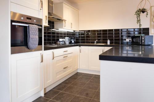 a kitchen with white cabinets and black tiles at Central Apartment- Stunning Sea Views- 100m to Beach- Sleeps 6 in Newquay