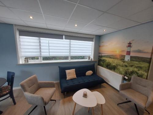 a living room with a blue couch and a lighthouse painting at 't Vakansie'uus in Serooskerke