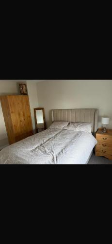 a bedroom with a white bed and a wooden cabinet at Ballycastle, Strand Cottages Modern Home in Ballycastle