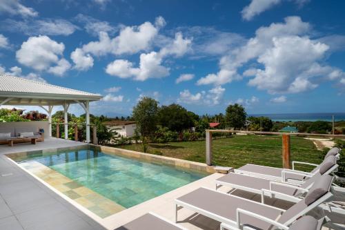 a swimming pool with white lounge chairs and a villa at Villa Joséphine in Grand-Bourg