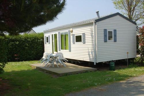 a small white tiny house with two people sitting on a porch at Camping 3 étoiles - Piscine - à 2 minutes des plages in Penvénan