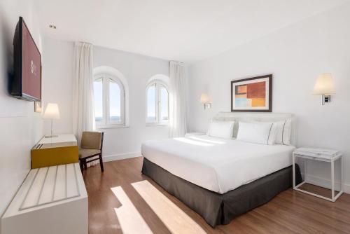 a white bedroom with a large bed and a chair at Dorma Victoria Palace in San Lorenzo de El Escorial