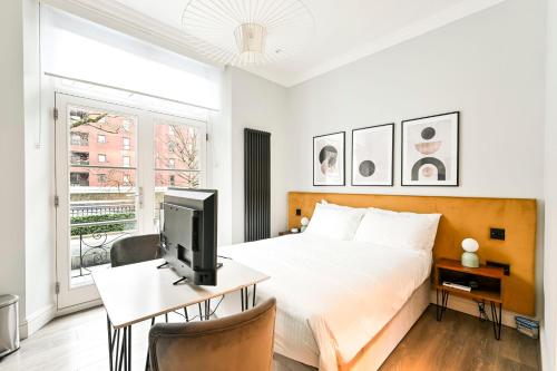 a bedroom with a bed and a desk with a television at The Collection Stays Chelsea in London