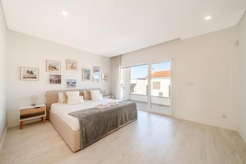 a white bedroom with a bed and a large window at GuestReady - Aroeira Pool Villa in Setúbal