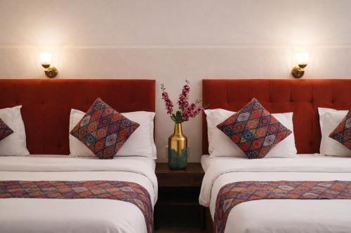 two beds in a hotel room with a vase of flowers at Saffron Inn - Near India Expo Mart in Greater Noida