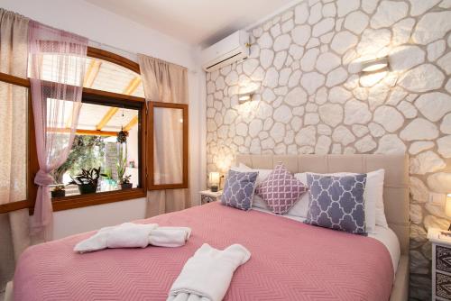 a bedroom with a pink bed with pillows and a window at Kiki's Apartments in Barbati