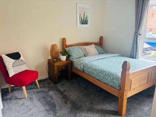 a bedroom with a bed and a red chair at Modern Ground floor 2 Bed Apartment Secure Parking & Perfect for City- CelticEmirates Stadium in Glasgow