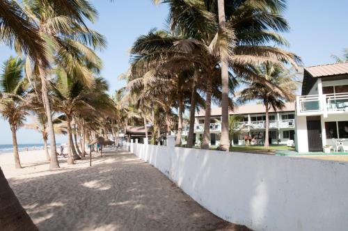 a white wall next to a beach with palm trees at Bungalow Beach Hotel in Serekunda