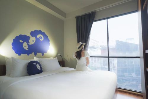 a woman standing next to a bed looking out a window at Kokotel Bangkok Surawong in Bangkok