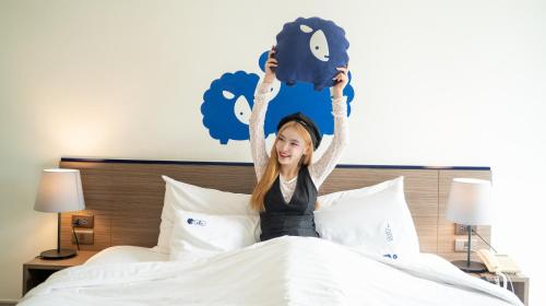 a woman is sitting on a bed holding up a phone at Kokotel Chiang Mai Nimman in Chiang Mai