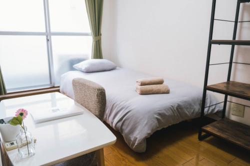 a room with a bed with a table and a shelf at Osaka English House in Hirakata