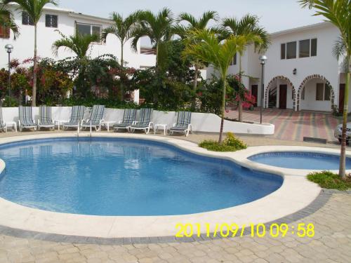 a pool with chairs and palm trees in front of a house at Hosteria Palmetto in Playas