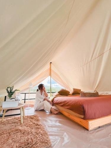 a woman sitting next to a bed in a tent at Mondara Villa and Glamping in Ban Bo Wi
