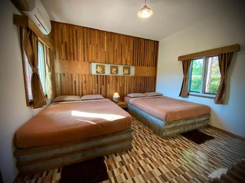 two beds in a bedroom with wooden walls and windows at Sarita Resort Villa in Kampong Huaibū