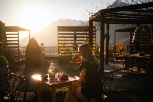 a woman sitting at a table with a drink at Landpalais Goyenhof - Deluxe Suites & Breakfast in Schenna