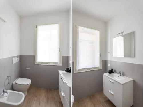 a bathroom with a toilet and sink and two windows at Maison Bellini 2 in Toscolano Maderno