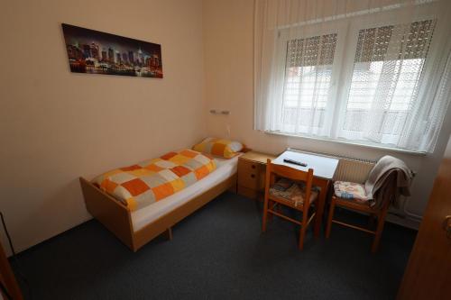 a small bedroom with a bed and a desk and a window at Pension Central in Bad Endbach