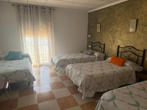 a hotel room with three beds and a window at Hostal Cabañas in Carboneras de Guadazaón