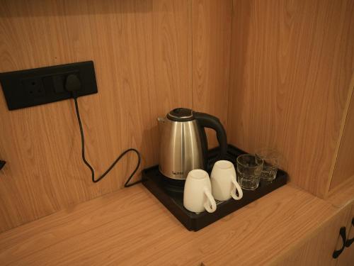 a tea kettle and some cups on a shelf at The RaaS Guestline in Noida