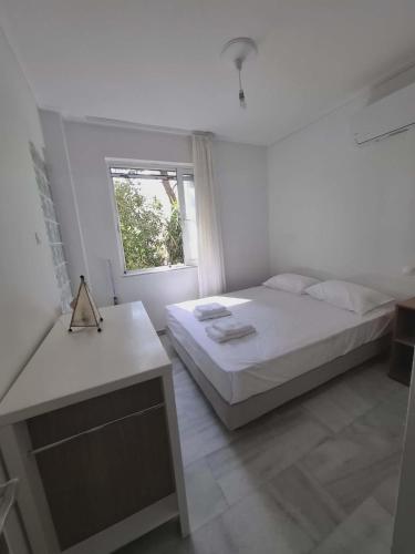 a white bedroom with a bed and a window at Varkiza Pines Apartment in Varkiza