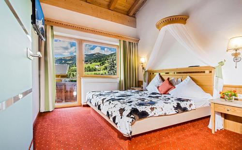ein Schlafzimmer mit einem Bett und einem großen Fenster in der Unterkunft Hotel Das Kohlmais - direkt an der Kohlmaisbahn JOKERCARD inklusive in Saalbach-Hinterglemm