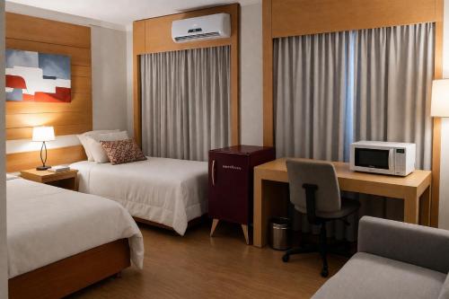 a hotel room with two beds and a desk with a computer at Flat próximo ao Aeroporto Congonhas Piscina, Academia e Restaurante in São Paulo