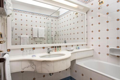 a bathroom with a sink and a tub and a mirror at Grand Hotel de la Ville in Sorrento