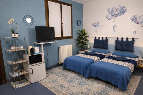 two beds in a bedroom with blue walls and a tv at La Casa Blu- Forum di Assago, Humanitas, Milanofiori, IEO in Rozzano