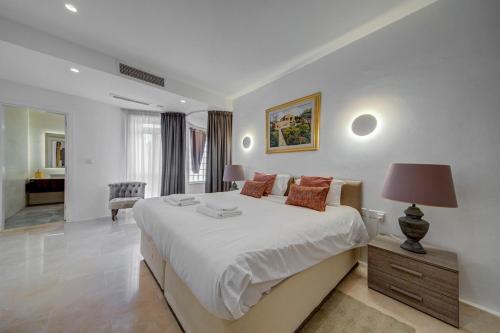 a white bedroom with a large bed and a chair at Vista Laguna - Harbour View - Private Jacuzzi in Għajnsielem