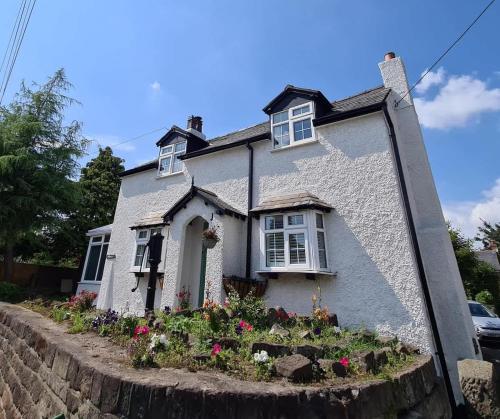 a white house with flowers in front of it at Gem of a cottage Close to Chester Chester Zoo in Mickle Trafford