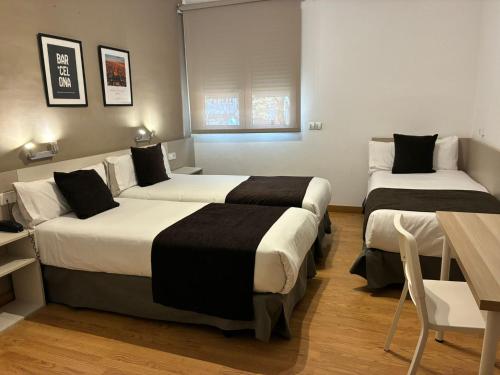 two beds in a hotel room with a table and chairs at Hotel Travessera in Barcelona