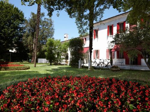 a garden of red flowers in front of a white building at Hotel Villa Patriarca - Buongiorno! Hotels in Mirano
