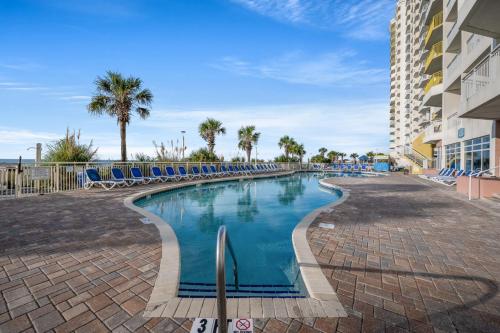 a swimming pool with chairs and palm trees and a building at Oceanfront Bay Watch 1BR with Resort Amenities 1707 in Myrtle Beach