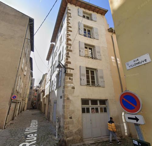 a man standing next to a building on a street at Les Suites Villeneuve - 2 in Le Puy-en-Velay