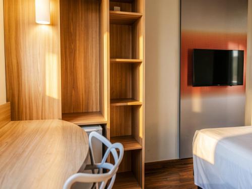 a hotel room with a bed and a tv and shelves at Aera São José Floripa - Hotel com café da manhã a 10 min do CentroSul in São José