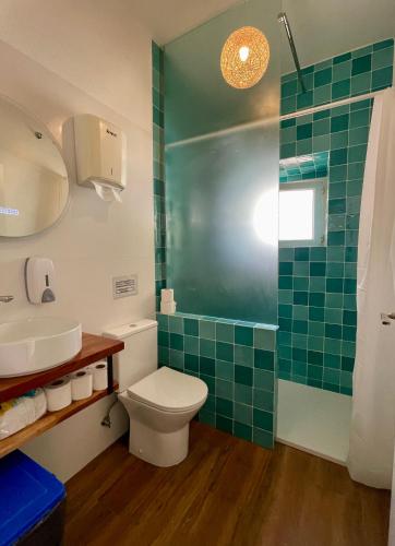 a bathroom with a toilet and a green tiled shower at Native Surfhouse in Praia da Areia Branca