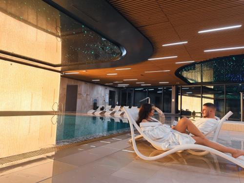 a man and woman sitting in chairs next to a swimming pool at Wave Apartments by Solarento in Międzyzdroje