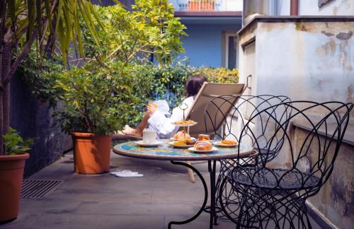 a woman sitting on a patio with a table with food on it at Shalai - Exclusive SPA and small gourmet hotel in Linguaglossa