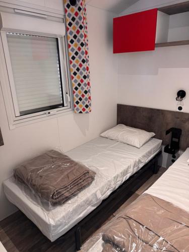 two beds in a room with a window at mobil home spacieux climatisé sur camping sol a gogo in Saint-Hilaire-de-Riez