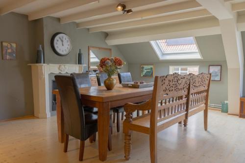 a dining room table with chairs and a clock on the wall at Bij Ons Achter in Biggekerke