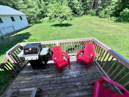 two red chairs and a grill on a deck at Cozy Retreat with Private Backyard Oasis in Livermore Falls